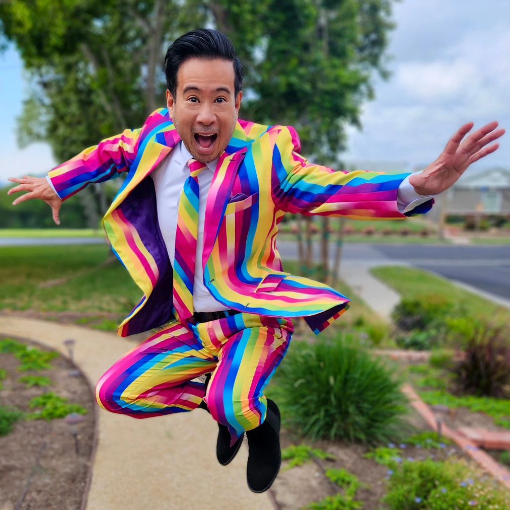 Ein Typ in einem Opposuits-Regenbogenglasuranzug springt mit weit geöffnetem Mund