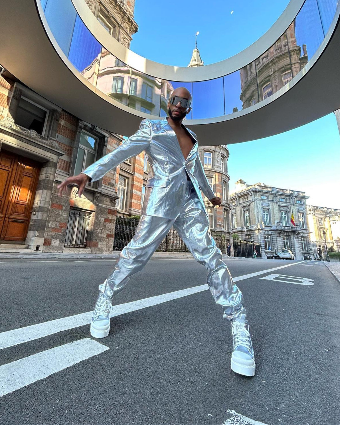 Person in einem silbernen reflektierenden Outfit posiert auf einer Stadtstraße.
