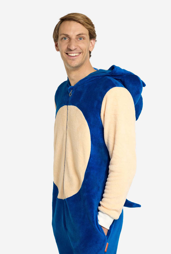 Ein Mann trägt einen verspielten blau-beigen Sonic the Hedgehog-Onesie für Erwachsene von OppoSuits. Der kuschelige Onesie hat einen Reißverschluss vorne und eine angenähte Kapuze, die Sonics ikonisches Gesicht mit Ohren und ausdrucksstarkem Blick nachempfunden ist. Der blaue Körper des Anzugs kontrastiert mit dem beigen Bauch und imitiert Sonics klassischen Look. Der Mann steht seitlich und blickt in die Kamera.