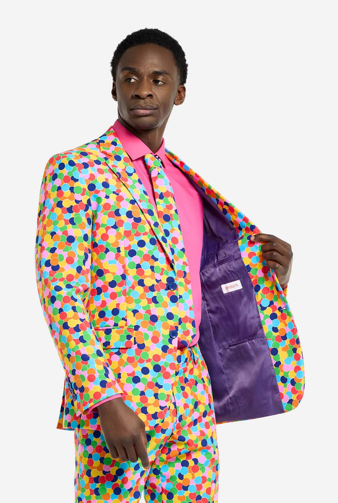 Bild eines Mannes, der einen OppoSuits Confetteroni-Herrenanzug mit Konfetti-Aufdruck und rosa Herrenhemd trägt. Der Anzug besteht aus Hose, Jacke und Krawatte.
