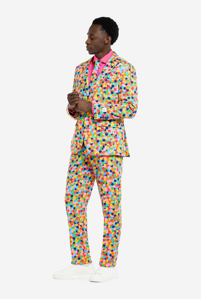 Bild eines Mannes, der einen OppoSuits Confetteroni-Herrenanzug mit Konfetti-Aufdruck und rosa Herrenhemd trägt. Der Anzug besteht aus Hose, Jacke und Krawatte.