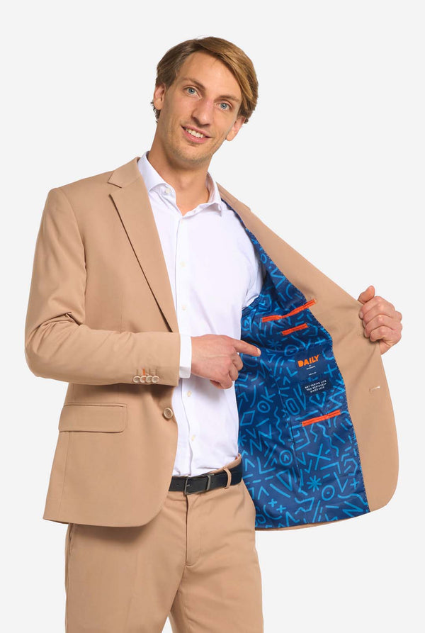 Bild mit hellgrauem Hintergrund und Mann trägt Dark Sand Herrenanzug und weißes Hemd. Anzüge besteht aus Blazer und Hose. Er hält eine Seite seiner Jacke offen.