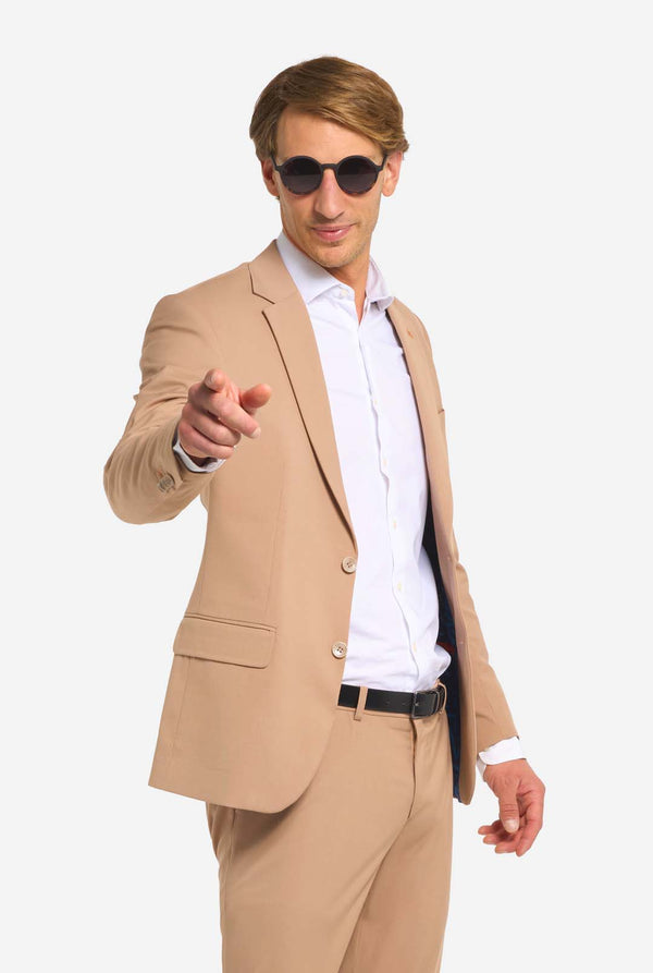Bild mit hellgrauem Hintergrund und Mann mit Sonnenbrille, Dark Sand Herrenanzug und weißes Hemd. Anzug besteht aus Blazer und Hose. Zeigt auf die Kamera.