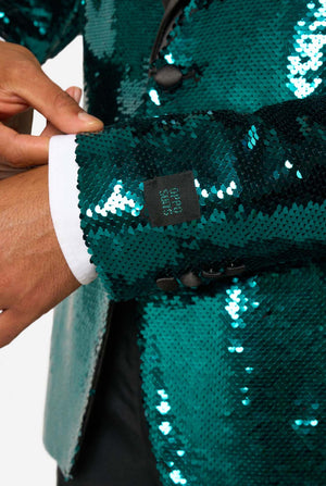 Ein Mann trägt einen türkis-glitzernden Blazer mit schwarzem Satin-Kragen.