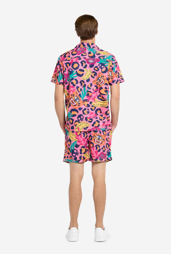 Ein Mann trägt ein farbenfrohes zweiteiliges Sommeroutfit mit auffälligem Tropenmuster. Das kurzärmelige Hemd und die dazu passenden Shorts präsentieren ein lebendiges Design mit neonpinken, orangefarbenen und gelben Leopardenmustern, Bananen, grünen Palmblättern und witzigen Cartoon-Gesichtern. Das Outfit ist lässig mit einem grünen T-Shirt darunter gestylt und perfekt für Sommerpartys, Urlaub oder Poolspaß. Ansicht von hinten.