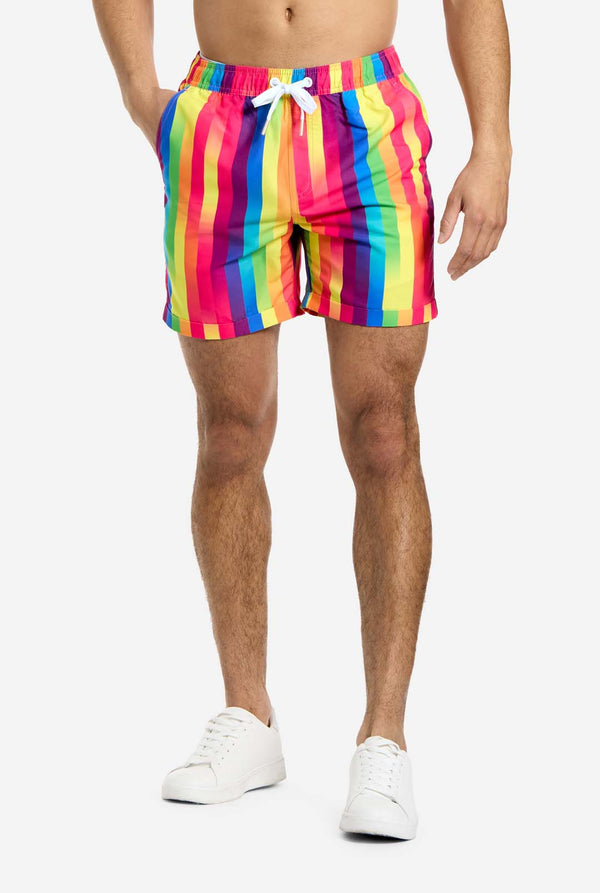 Ein Mann trägt Shorts mit vertikalen Streifen in Regenbogenfarben. Er hält eine Hand in der Hosentasche. Nur der untere Teil seines Körpers ist zu sehen.
