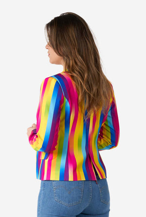 Bild einer Frau in einem vertikal gestreiften, regenbogenfarbenen Blazer, einem weißen Hemd und blauen Jeans. Sie hält die Seiten des Blazers. Ansicht von hinten.