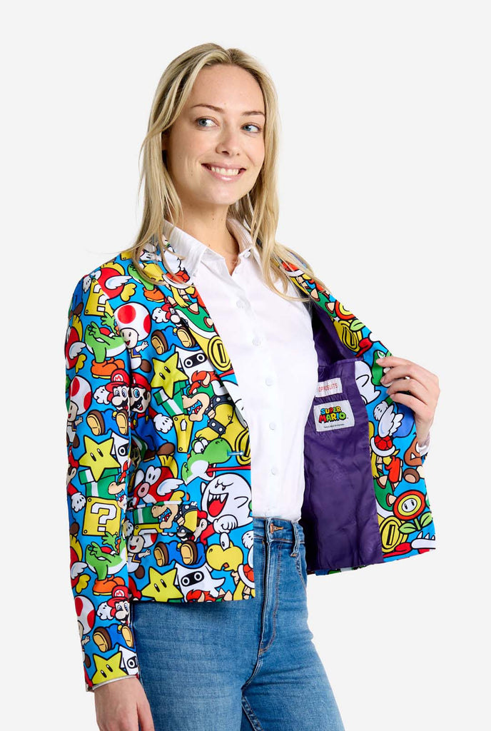 Frau trägt einen Super Mario-Blazer mit Allover-Print und ikonischen Super Mario-Figuren. Die Basis ist hellblau, aber es gibt auch Gelb, Rot und Weiß.