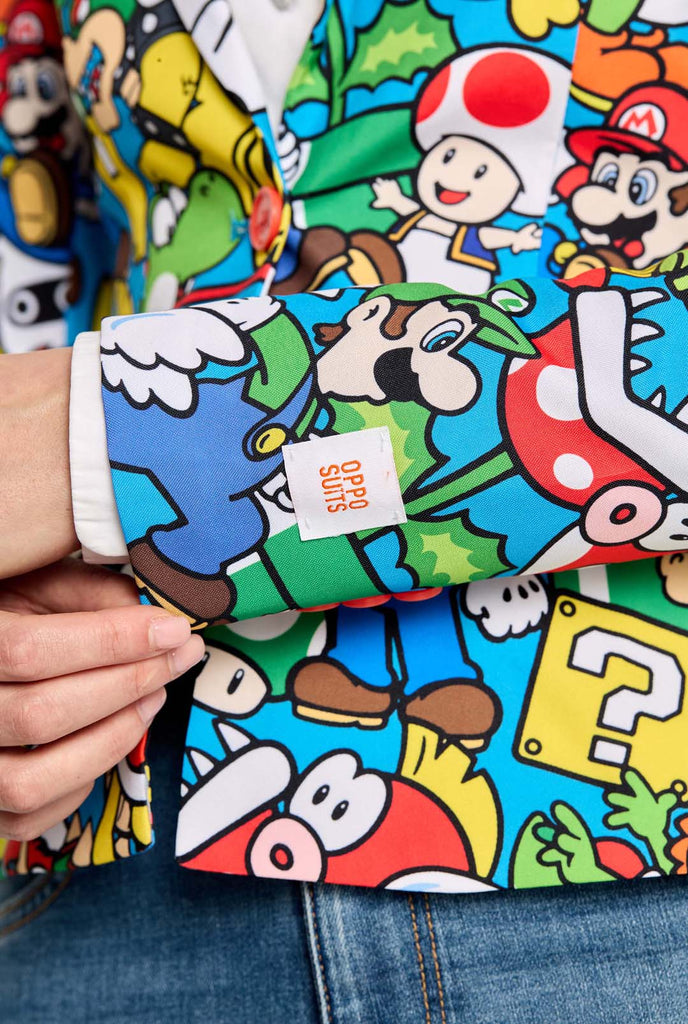 Frau trägt einen Super Mario-Blazer mit Allover-Print und ikonischen Super Mario-Figuren. Die Basis ist hellblau, aber es gibt auch Gelb, Rot und Weiß.