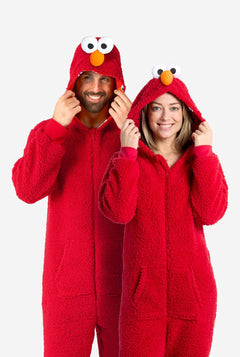 Ein Mann und eine Frau tragen einen roten Elmo-Einteiler. Das Design imitiert den Look der Sesamstraßenfigur Elmo. Der Hintergrund ist schlicht, wodurch das Kostüm besonders hervorgehoben wird. Ganzkörperaufnahme.