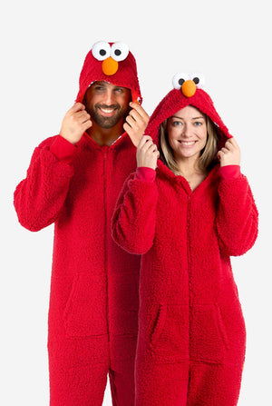 Ein Mann und eine Frau tragen einen roten Elmo-Einteiler. Das Design imitiert den Look der Sesamstraßenfigur Elmo. Der Hintergrund ist schlicht, wodurch das Kostüm besonders hervorgehoben wird. Ganzkörperaufnahme.