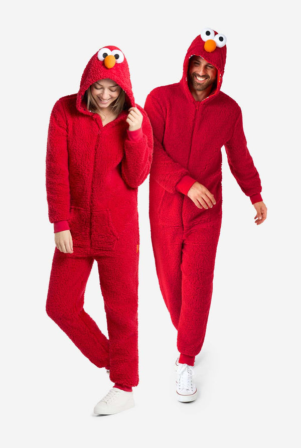 Ein Mann und eine Frau tragen einen roten Elmo-Einteiler. Das Design imitiert den Look der Sesamstraßenfigur Elmo. Der Hintergrund ist schlicht, wodurch das Kostüm besonders hervorgehoben wird. Ganzkörperaufnahme.