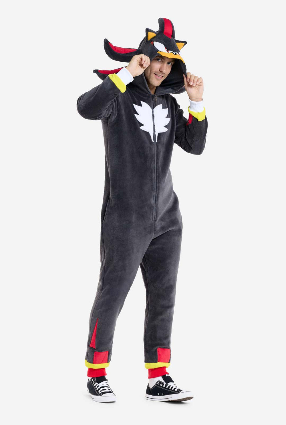 Ein Mann, der einen schwarzen Plüsch-Onesie trägt, der von der beliebten Igel-Figur Shadow inspiriert ist, mit stacheligen roten und schwarzen Akzenten an der Kapuze, einem weißen Brustemblem und gelben Details an den Handgelenken. Der Strampler ist aus weichem Fleecematerial gefertigt und bietet Komfort und ein verspieltes Design für Cosplay, Faulenzen oder thematische Veranstaltungen. Die Person lächelt, während sie die Kapuze zurechtrückt, und zeigt dabei das erkennbare Gesicht und das auffällige Design 