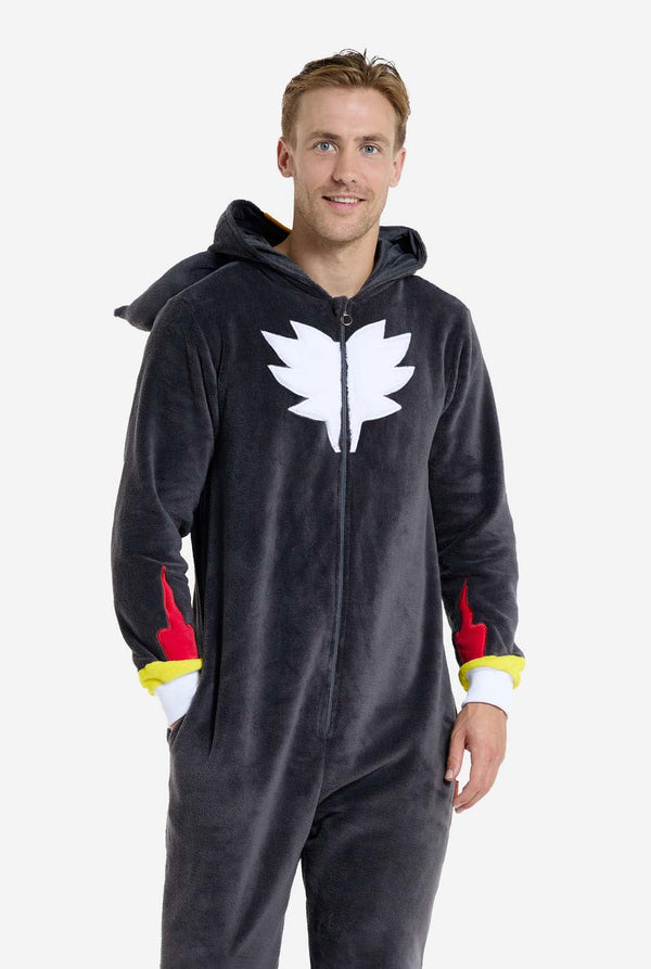 Ein Mann trägt einen plüschigen schwarzen Onesie, inspiriert vom beliebten Igel Shadow. Er besticht durch stachelige rote und schwarze Akzente an der Kapuze, ein weißes Brustemblem und gelbe Handgelenksdetails. Der Onesie aus weichem Fleece bietet Komfort und ein verspieltes Design für Cosplay, Lounge-Abende oder Themenveranstaltungen. Die Person lächelt, während die Kapuze auf ihrem Rücken liegt. Perfekt für Fans von Gaming- oder Zeichentrickfiguren.