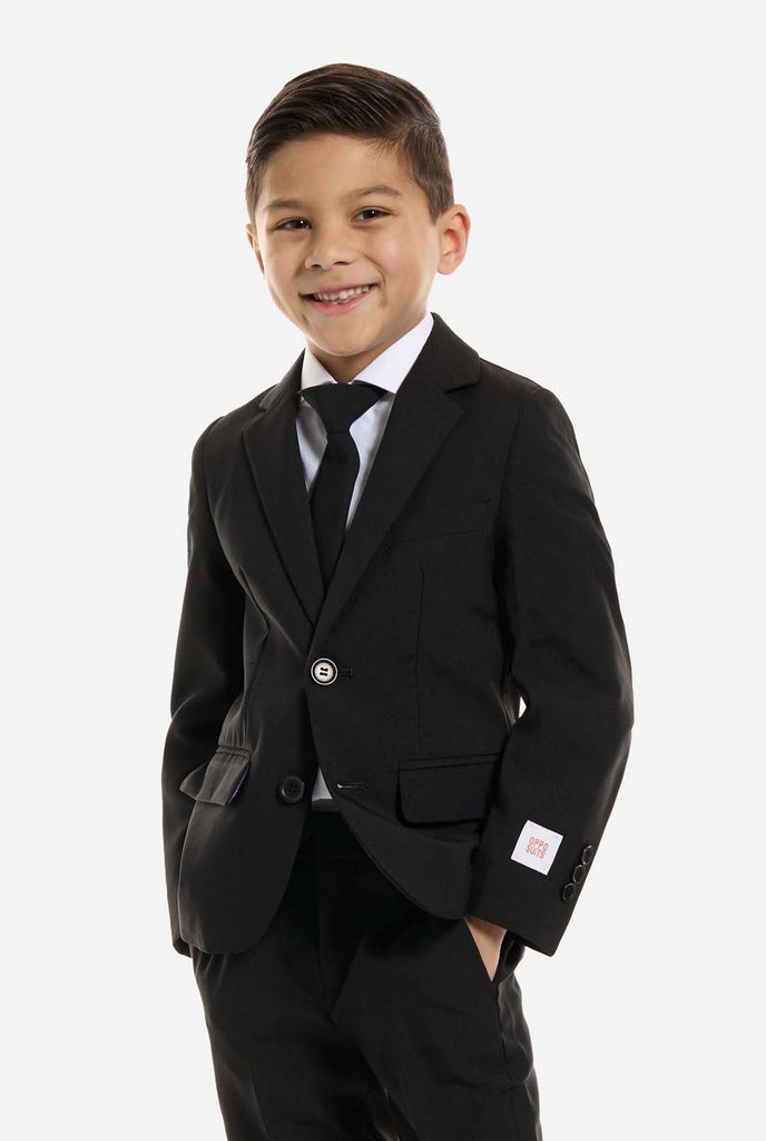 Der Junge trägt einen schwarzen Anzug von OppoSuits.