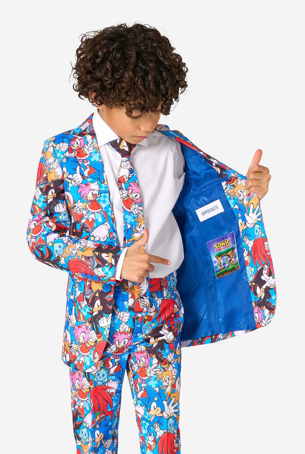 Junge in einem farbenfrohen Sonic-Teenie-Anzug mit bunten Aufdrucken von Sonic the Hedgehog-Figuren wie Sonic, Knuckles, Tails und Amy, gepaart mit einer passenden Krawatte und einem weißen Hemd. Hält eine Seite seiner Jacke offen.