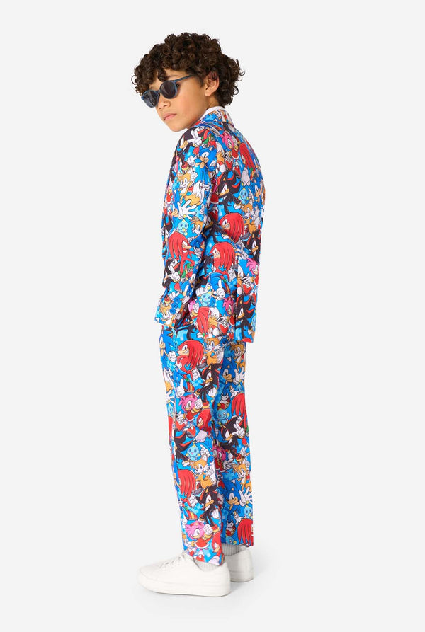 Junge mit Sonnenbrille und einem farbenfrohen Sonic-Teenie-Anzug mit bunten Aufdrucken von Sonic the Hedgehog-Figuren wie Sonic, Knuckles, Tails und Amy, gepaart mit einer passenden Krawatte und einem weißen Hemd. Seitenansicht.