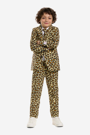 Auf diesem Bild trägt ein Kind einen Jungenanzug mit Panther-Allover-Print und weißem Hemd. Der Anzug ist beige mit braun-schwarz geflecktem Panther-Print. Der Anzug besteht aus Jacke, Hose und Clip-On-Krawatte.