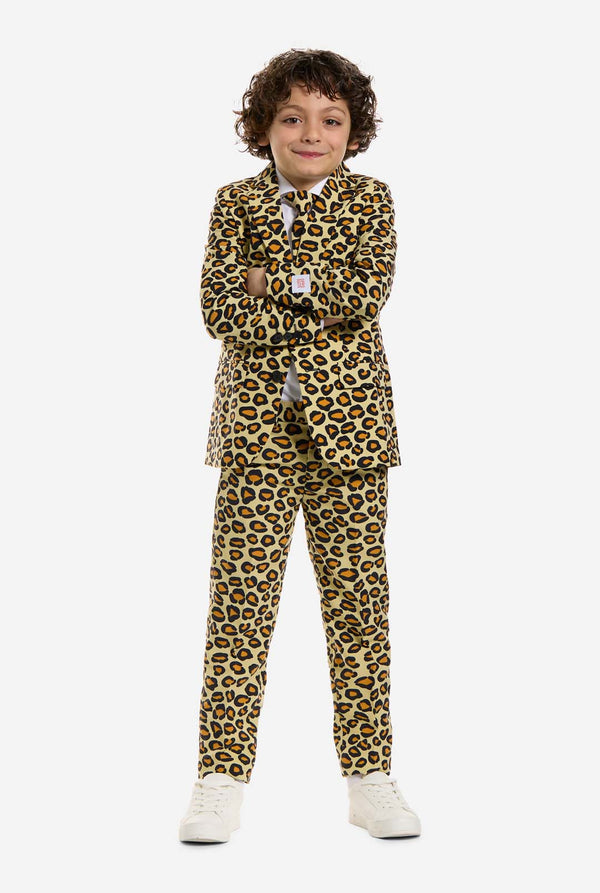 Auf diesem Bild trägt ein Kind einen Jungenanzug mit Panther-Allover-Print und weißem Hemd. Der Anzug ist beige mit braun-schwarz geflecktem Panther-Print. Der Anzug besteht aus Jacke, Hose und Clip-On-Krawatte.