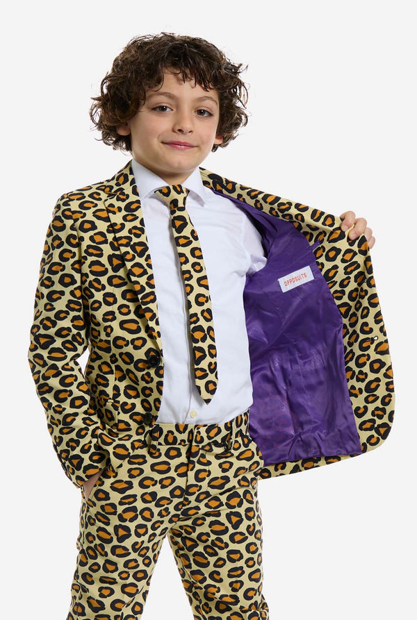 Auf diesem Bild trägt ein Kind einen Jungenanzug mit Panther-Allover-Print und weißem Hemd. Der Anzug ist beige mit braun-schwarz geflecktem Panther-Print. Der Anzug besteht aus Jacke, Hose und Clip-On-Krawatte.