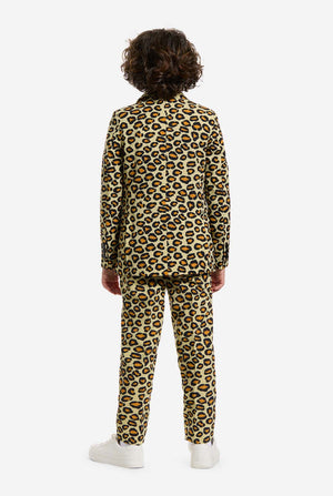 Auf diesem Bild trägt ein Kind einen Jungenanzug mit Panther-Allover-Print und weißem Hemd. Der Anzug ist beige mit braun-schwarz geflecktem Panther-Print. Der Anzug besteht aus Jacke, Hose und Clip-On-Krawatte.