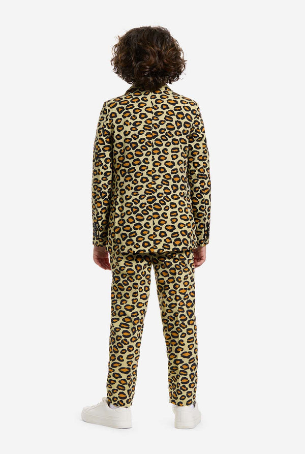 Auf diesem Bild trägt ein Kind einen Jungenanzug mit Panther-Allover-Print und weißem Hemd. Der Anzug ist beige mit braun-schwarz geflecktem Panther-Print. Der Anzug besteht aus Jacke, Hose und Clip-On-Krawatte.