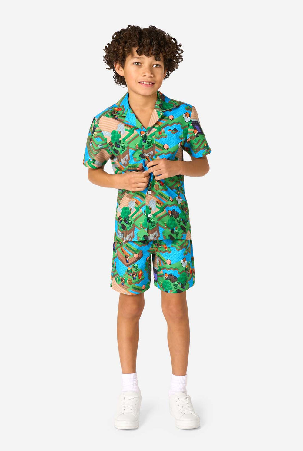 Ein Junge trägt ein buntes Sommeroutfit mit einem Minecraft-Overworld-Motiv, das pixelige Landschaften, Charaktere und Elemente aus dem ikonischen Spiel zeigt. Das kurzärmelige Hemd und die passenden Shorts heben ein lebhaftes Design hervor, das von der Minecraft-Welt inspiriert ist.