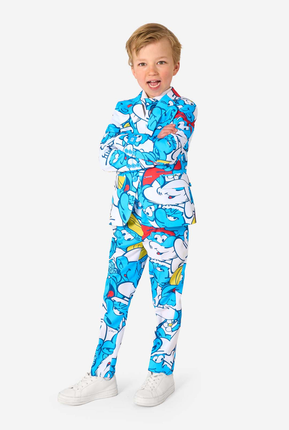 Junger Junge trägt einen bunten Kinderanzug mit Schlumpf-Motiv, der lebendige blaue Cartoon-Figuren zeigt, inklusive Jacke, Hose und passender Krawatte, lächelt vor einem schlichten weißen Hintergrund.