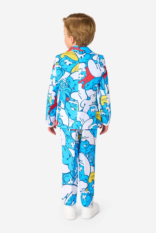 Junger Junge trägt einen bunten Kinderanzug mit Schlumpf-Motiv, der lebendige blaue Cartoon-Figuren zeigt, inklusive Jacke, Hose und passender Krawatte, lächelt vor einem schlichten weißen Hintergrund. Ansicht von hinten.