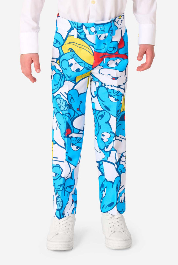 Junger Junge trägt einen bunten Kinderanzug mit Schlumpf-Motiv, der lebendige blaue Cartoon-Figuren zeigt, inklusive Jacke, Hose und passender Krawatte, lächelt vor einem schlichten weißen Hintergrund. Nahaufnahme der Hose.