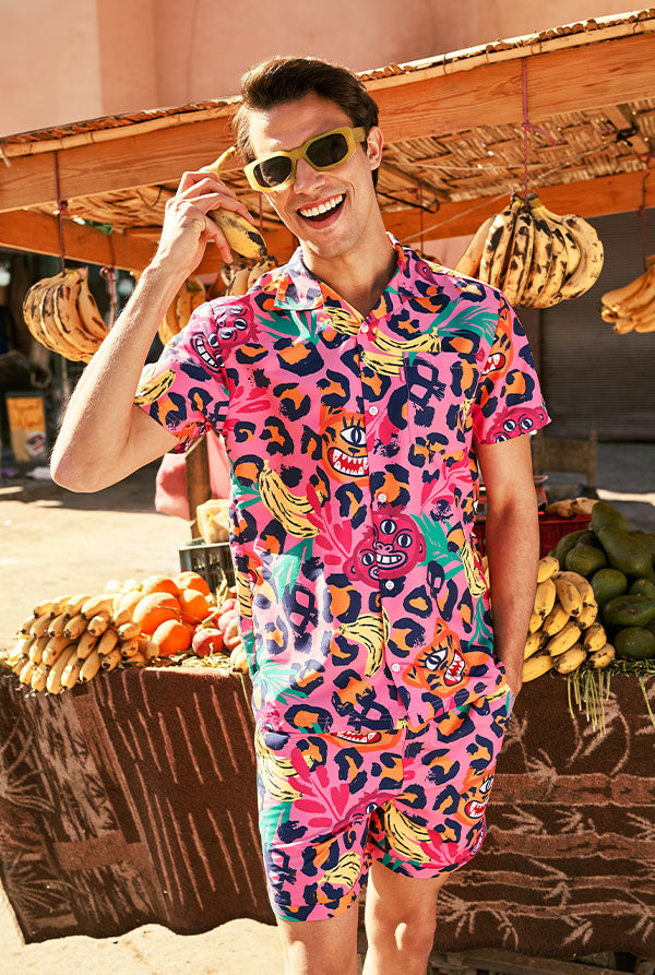 Person in farbenfrohem Outfit mit lebhaftem Muster steht vor einem Obststand.
