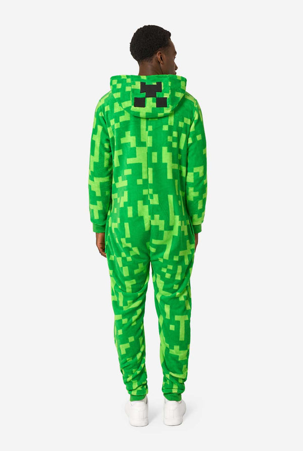 Ein Mann, der einen grünen, pixeligen Einteiler trägt, der wie der Minecraft Creeper-Charakter aussehen soll. Der Strampler hat eine Kapuze mit dem ikonischen schwarzen Pixelgesicht des Creepers. Der Mann hat die Kapuze auf dem Rücken. Ansicht von hinten.