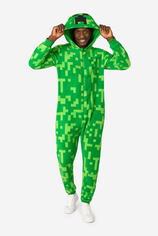 Ein Mann, der einen grünen, pixeligen Einteiler trägt, der wie der Minecraft Creeper-Charakter aussehen soll. Der Strampler hat eine Kapuze mit dem ikonischen schwarzen Pixelgesicht des Creepers. Der Mann trägt die Kapuze und blickt in die Kamera