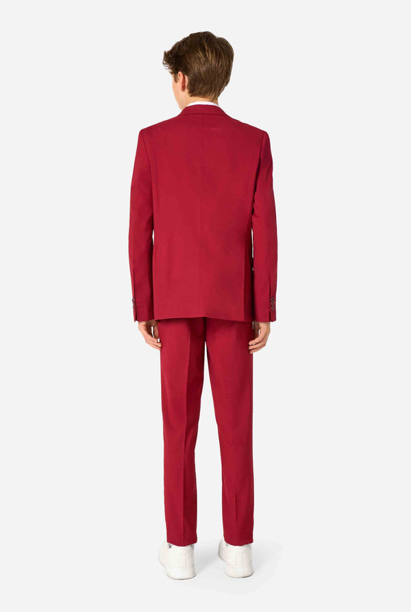 Teenager in einem eleganten burgunderroten Anzug mit weißem Hemd und selbstbewusstem Auftritt. Perfektes formelles Outfit für besondere Anlässe, Hochzeiten und Partys. Ansicht von hinten.