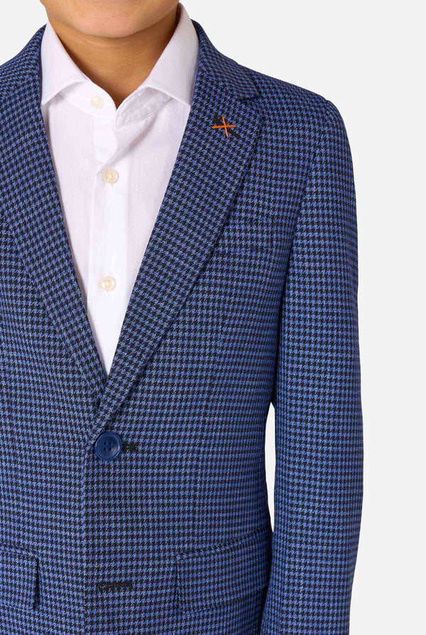 Ein Junge trägt einen dunkelblau-blau karierten Anzug und ein weißes Hemd. Der Anzug hat eine moderne Passform mit zwei Knöpfen und Pattentaschen. Er steht vor einem schlichten weißen Hintergrund. Nahaufnahme der Brust