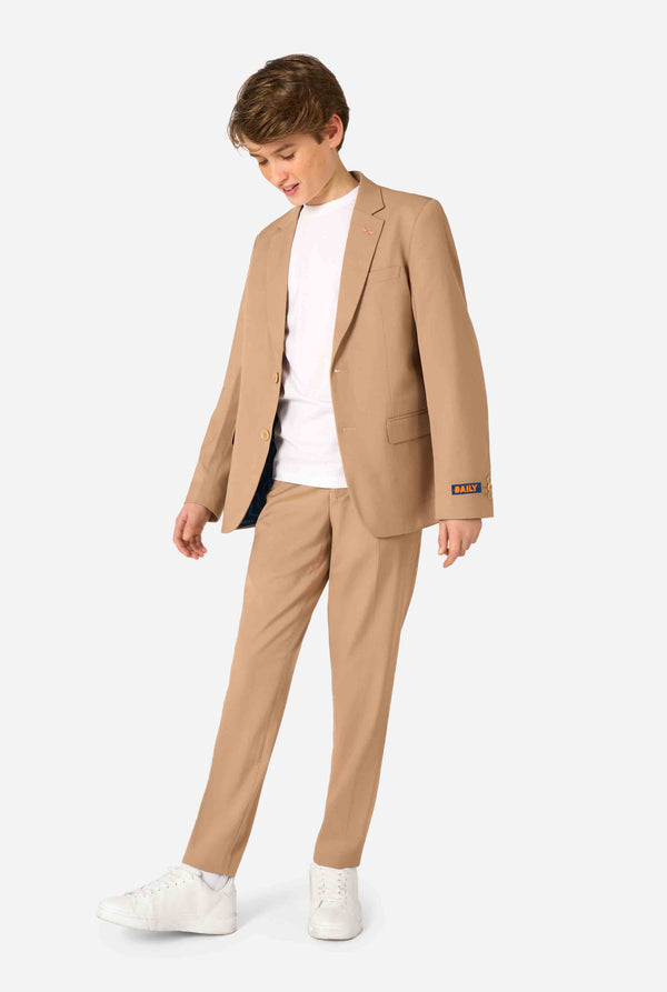 Teenager trägt einen stylischen hellbraunen/beigen Anzug mit weißem Hemd und wirkt selbstbewusst. Perfektes formelles Outfit für besondere Anlässe, Hochzeiten und Partys. Ganzkörperfoto.