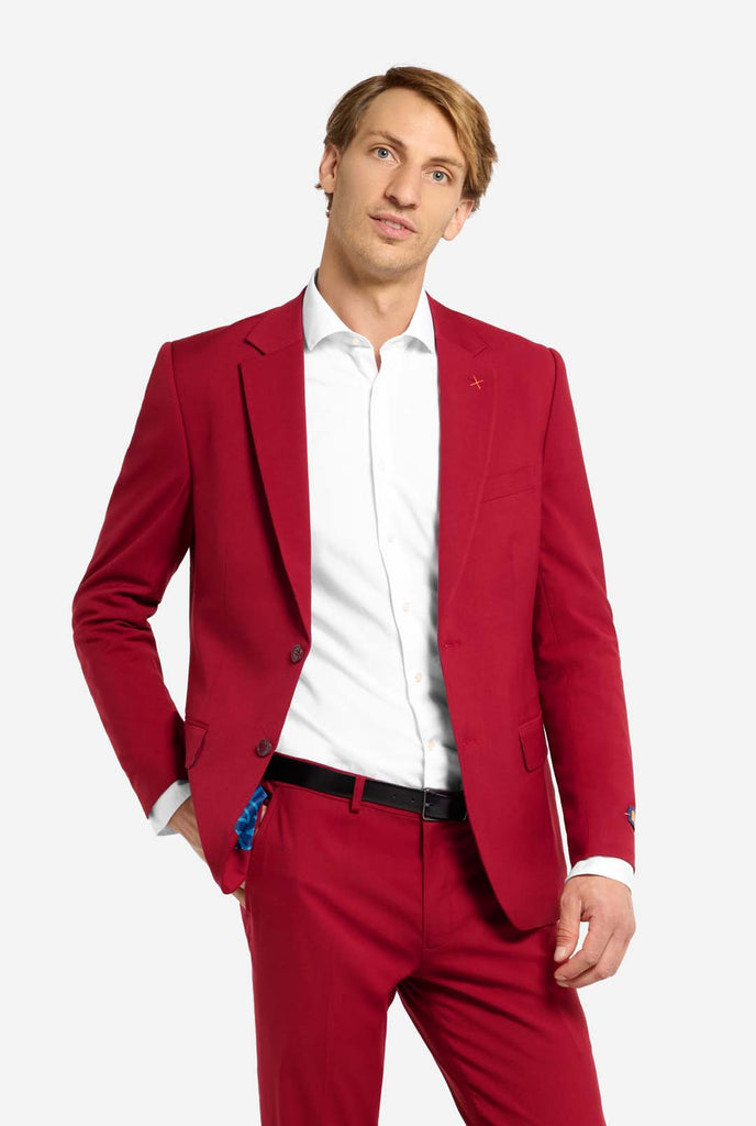 Bild mit hellgrauem Hintergrund und Mann trägt Bright Burgundy Herrenanzug und weißes Hemd. Anzug besteht aus Blazer und Hose. Mann schaut in die Kamera, Ganzkörperbild.