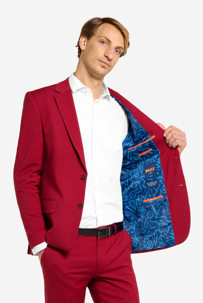 Bild mit hellgrauem Hintergrund und Mann trägt Bright Burgundy Herrenanzug und weißes Hemd. Anzüge besteht aus Blazer und Hose. Er hält eine Seite seiner Jacke offen.