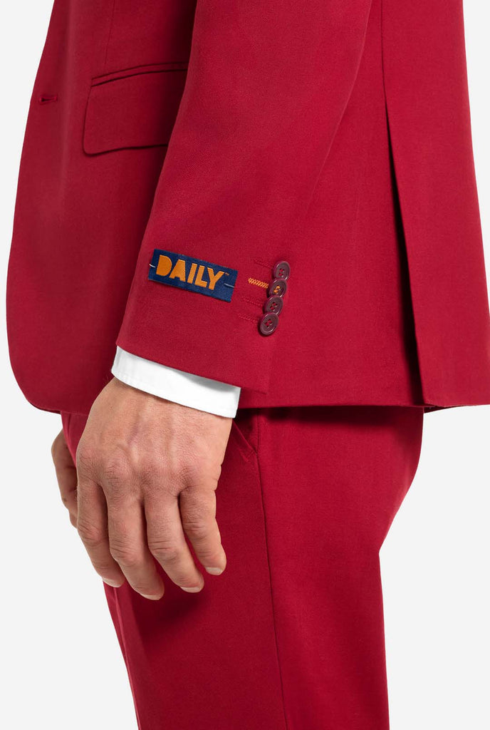 Bild mit hellgrauem Hintergrund und Mann trägt Bright Burgundy Herrenanzug und weißes Hemd. Der Anzug besteht aus Blazer und Hose. Ansicht von der Seite.