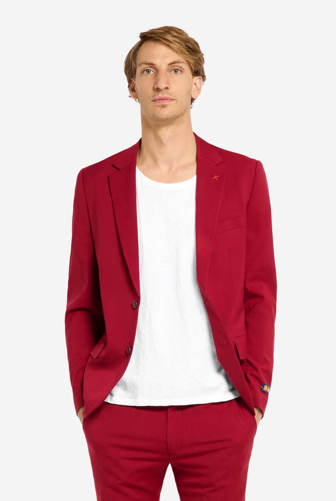 Bild mit hellgrauem Hintergrund und Mann trägt Bright Burgundy Herrenanzug und weißes Hemd. Anzüge besteht aus Blazer und Hose. Mann schaut in die Kamera.