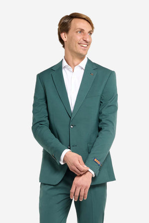 Bild mit hellgrauem Hintergrund und einem Mann in dunkelgrünem Anzug und weißem Hemd. Der Anzug besteht aus Blazer und Hose. Der Mann blickt zur Seite.