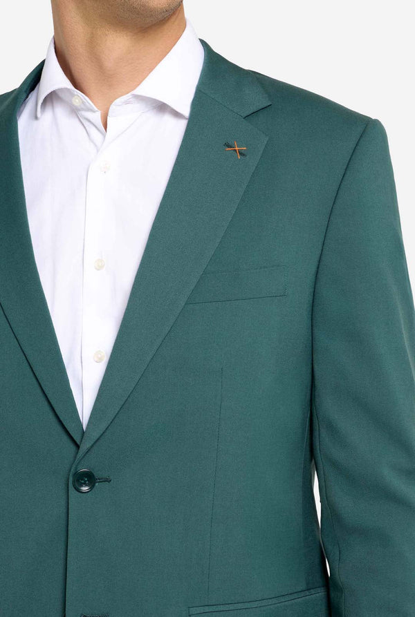 Bild mit hellgrauem Hintergrund und einem Mann in dunkelgrünem Anzug und weißem Hemd. Der Anzug besteht aus Blazer und Hose. Nahaufnahme der Brust.