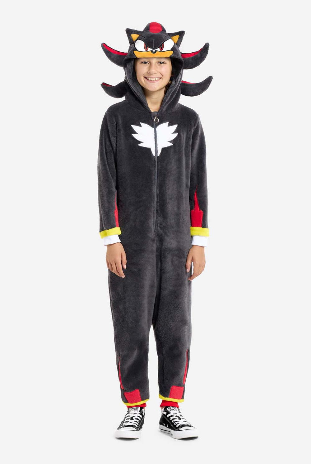 Ein Kind trägt einen schwarzen Plüsch-Onesie für Kinder, der von der beliebten Igel-Figur Shadow inspiriert ist. Er hat rote und schwarze Stacheln an der Kapuze, ein weißes Brustemblem und gelbe Details an den Handgelenken. Der Strampler ist aus weichem Fleecematerial gefertigt und bietet Komfort und ein verspieltes Design für Cosplay, Faulenzen oder thematische Veranstaltungen. Die Person lächelt, während die Kapuze auf ihrem Kopf sitzt. Perfekt für Fans von Spielen oder Zeichentrickfiguren.