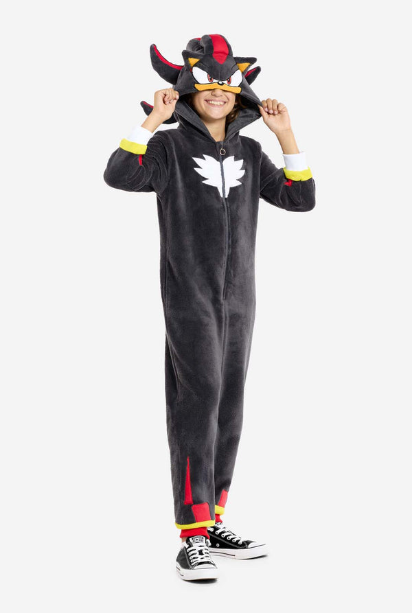 Ein Kind trägt einen plüschigen schwarzen Kinder-Onesie, inspiriert vom beliebten Igel Shadow. Er hat stachelige rote und schwarze Akzente an der Kapuze, ein weißes Brustemblem und gelbe Details am Handgelenk. Der Onesie aus weichem Fleece bietet Komfort und ein verspieltes Design für Cosplay, zum Entspannen oder für Themenveranstaltungen. Die Person lächelt, während sie die Kapuze zurechtrückt und so das bekannte Gesicht und das auffällige Design der Figur zum Vorschein bringt. 