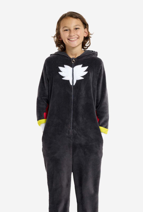 Ein Kind trägt einen plüschigen schwarzen Kinder-Onesie, inspiriert vom beliebten Igel Shadow. Er hat stachelige rote und schwarze Akzente an der Kapuze, ein weißes Brustemblem und gelbe Handgelenksdetails. Der Onesie aus weichem Fleece bietet Komfort und ein verspieltes Design für Cosplay, zum Entspannen oder für Themenveranstaltungen. Die Person lächelt, während die Kapuze auf dem Rücken liegt. Perfekt für Fans von Gaming- oder Zeichentrickfiguren.