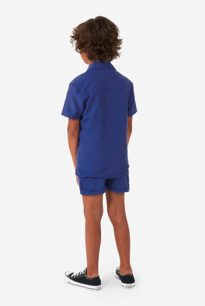 Junge trägt dunkelblaues Sommerset, bestehend aus Shorts und Hemd, Blick von hinten