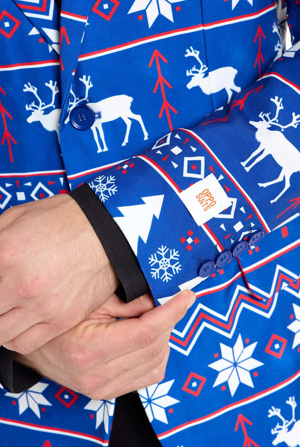 Mann trägt einen blauen Weihnachtsblazer für Herren mit nordischen Weihnachtsfiguren. Er trägt außerdem eine schwarze Hose und ein schwarzes Herrenhemd. Nahaufnahme der Ärmel.