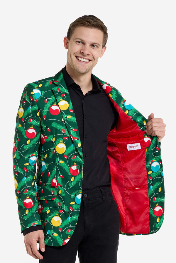 Mann trägt einen grünen Weihnachtsblazer für Herren mit verziertem Weihnachtsbaum-Aufdruck. Außerdem trägt er eine schwarze Hose und ein schwarzes Herrenhemd. Die Innenseite der Jacke ist rot.