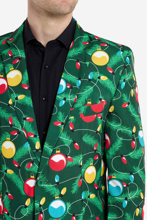 Mann trägt einen grünen Weihnachtsblazer für Herren mit verziertem Weihnachtsbaum-Aufdruck. Er trägt außerdem eine schwarze Hose und ein schwarzes Herrenhemd. Nahaufnahme der Brust.