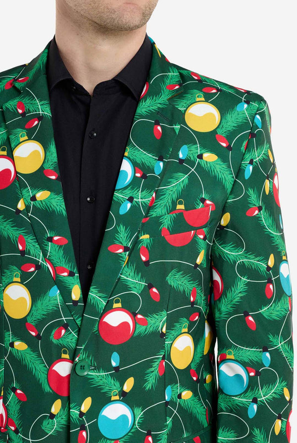 Mann trägt einen grünen Weihnachtsblazer für Herren mit verziertem Weihnachtsbaum-Aufdruck. Er trägt außerdem eine schwarze Hose und ein schwarzes Herrenhemd. Nahaufnahme der Brust.